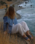 Woman wearing Theluto Gaelle leather slip-on sandals while sitting on a cliff overlooking the ocean