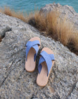 Theluto Gaelle blue leather slip-on sandals with a cushioned sole, displayed on a rocky cliff overlooking the sea.