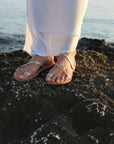 Theluto Lilou Glitter handcrafted leather sandals in gold, worn by a woman on a rocky shore.