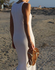 Woman in white dress holding Theluto Lilou Glitter leather sandals on a sandy beach at sunset