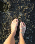 Theluto Lilou Glitter sandals with gold straps on feet, handcrafted from natural leather on a rocky surface
