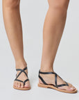Theluto Marie minimalist black leather sandals with thin crisscross straps and a flat tan sole on a model
