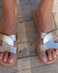 Theluto Prune handmade gold leather slip-on sandals with a chic minimalist crisscross strap design on wooden decking.