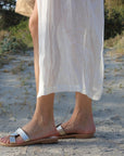 Theluto Prune handmade silver leather slip-on sandals worn by a woman in a white dress on a sandy beach path