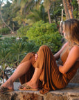 Theluto Gaelle Cheetah slip-on sandals with leopard print leather worn by a woman sitting on a stone wall at sunset