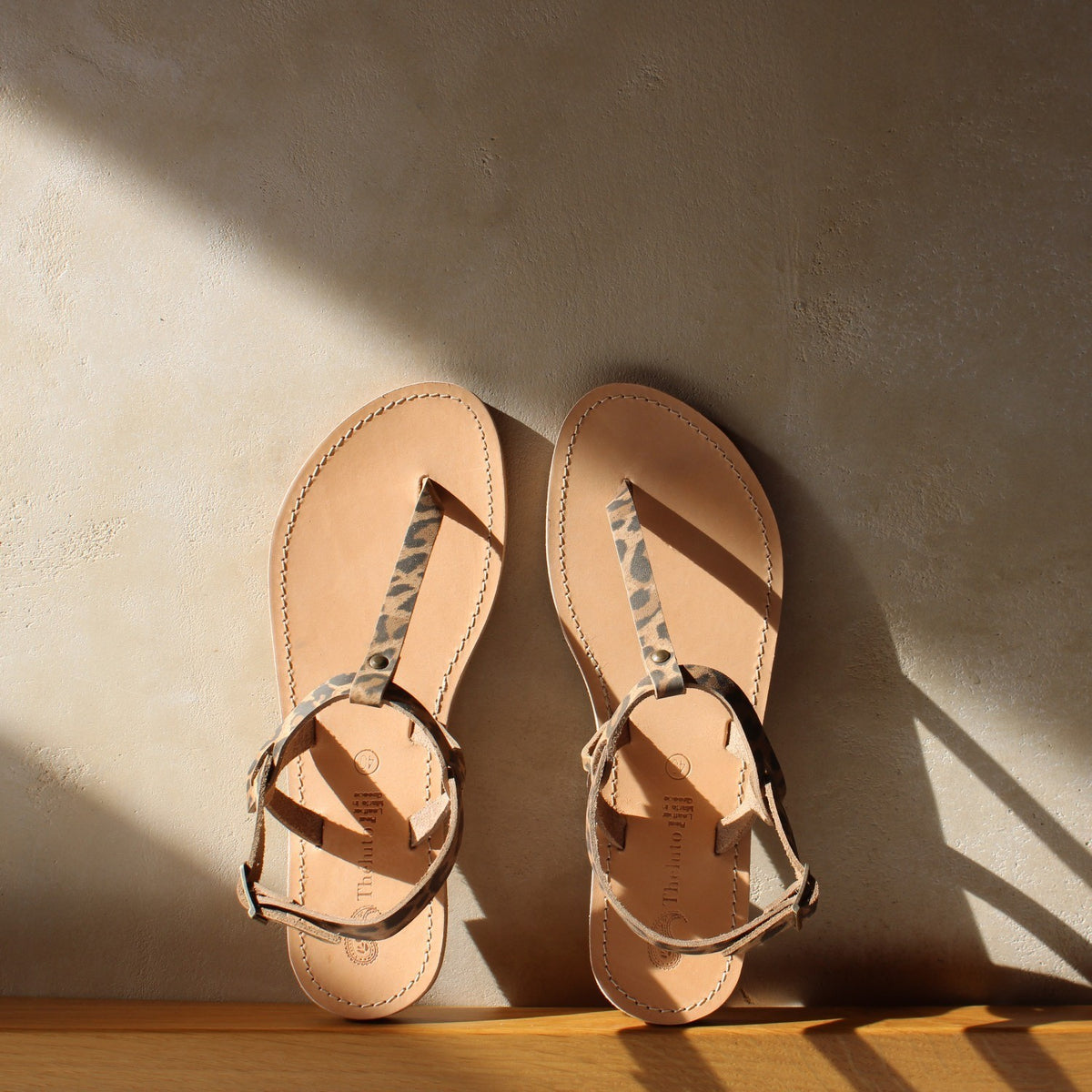 Theluto Meloe Cheetah leather sandals with leopard print straps and ankle ties on a neutral textured background