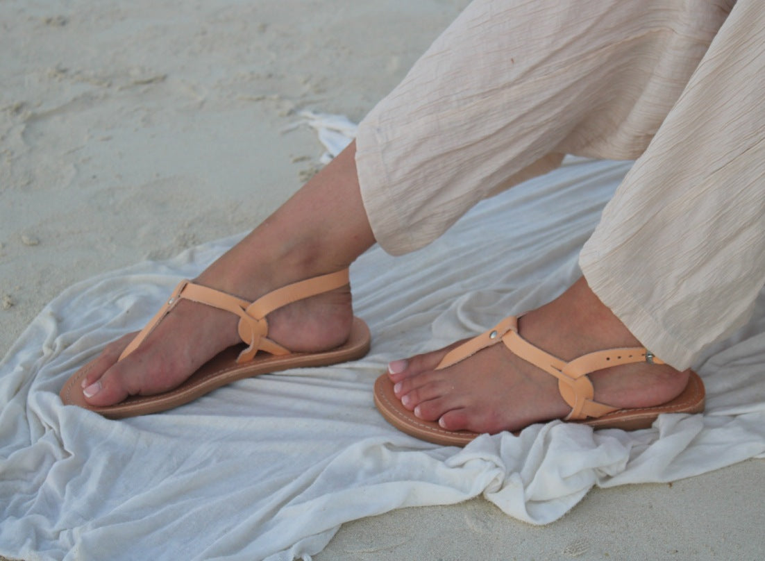 Theluto Meloe tan leather sandals with ankle ties worn on a sandy beach with light linen trousers