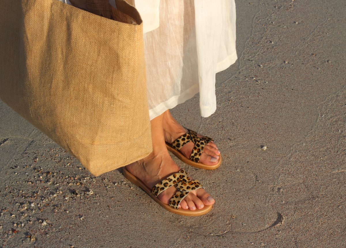 Theluto Prune Cheetah leather slip-on sandals with animal print, worn on a sandy beach with a linen dress and tote bag.